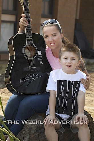 Courtney Rolins and her son Seth Rolins-Winfield, 8, with a Lee Kernaghan autograph guitar.